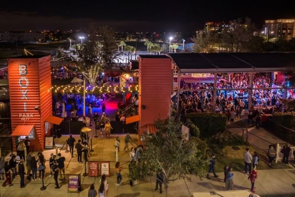 A nighttime aerial shot of two orange towers labeled Boxi Park, behind which lies a variety of food counters and a busy covered stage area.