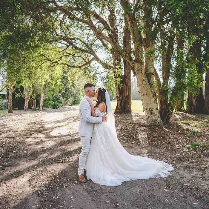 A couple in wedding attire embracing under a tree canopy at Mercure Kooindah Waters