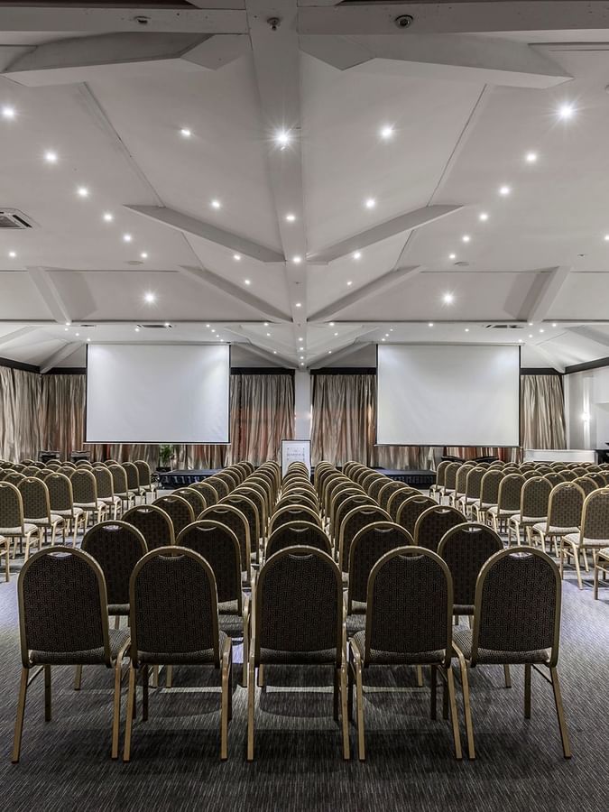 Vusu Boardroom with rows of chairs by two large screens under a white vaulted ceiling at Warwick Fiji Resort and Spa