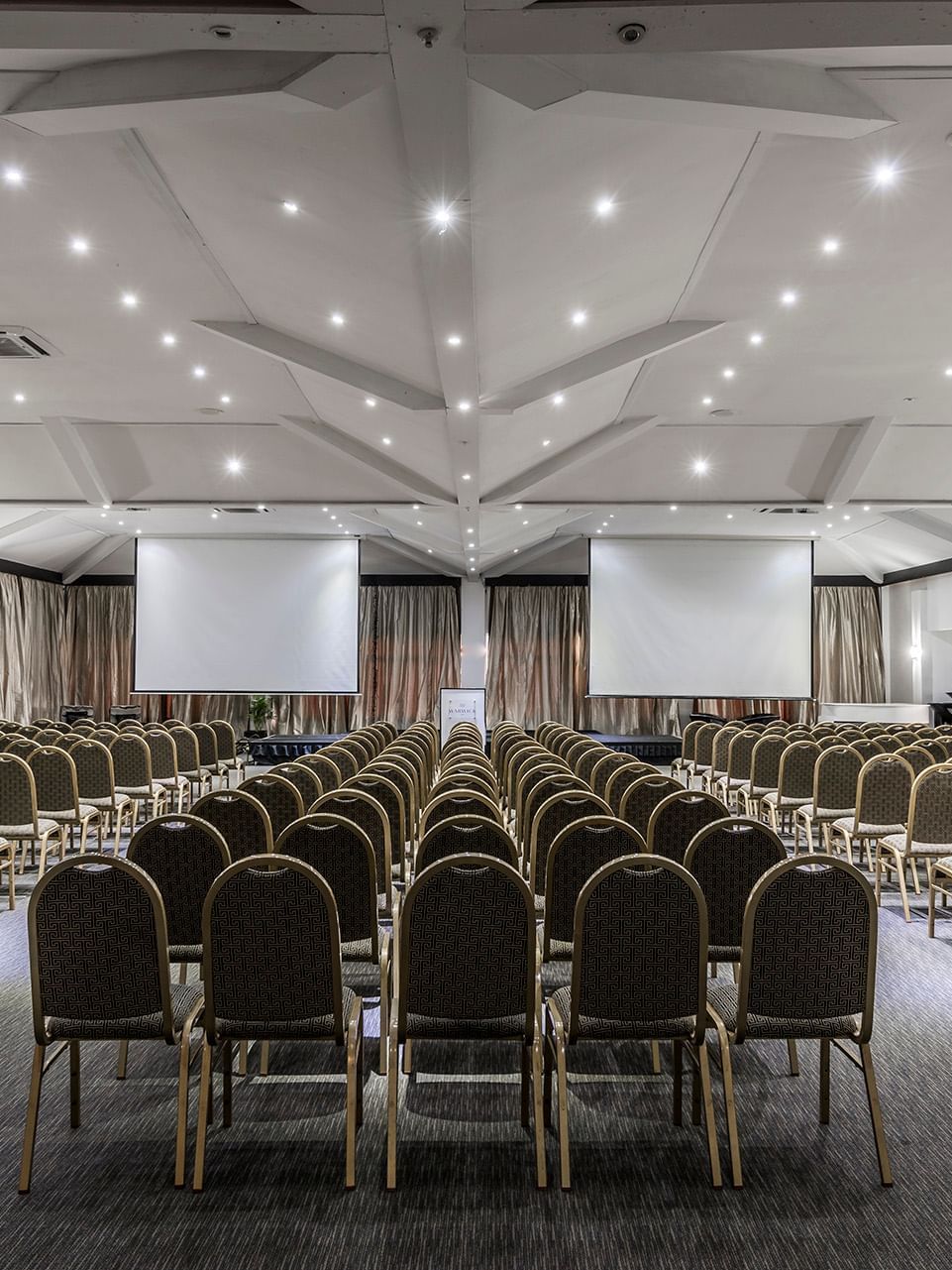 Vusu Boardroom with rows of chairs by two large screens under a white vaulted ceiling at Warwick Fiji Resort and Spa