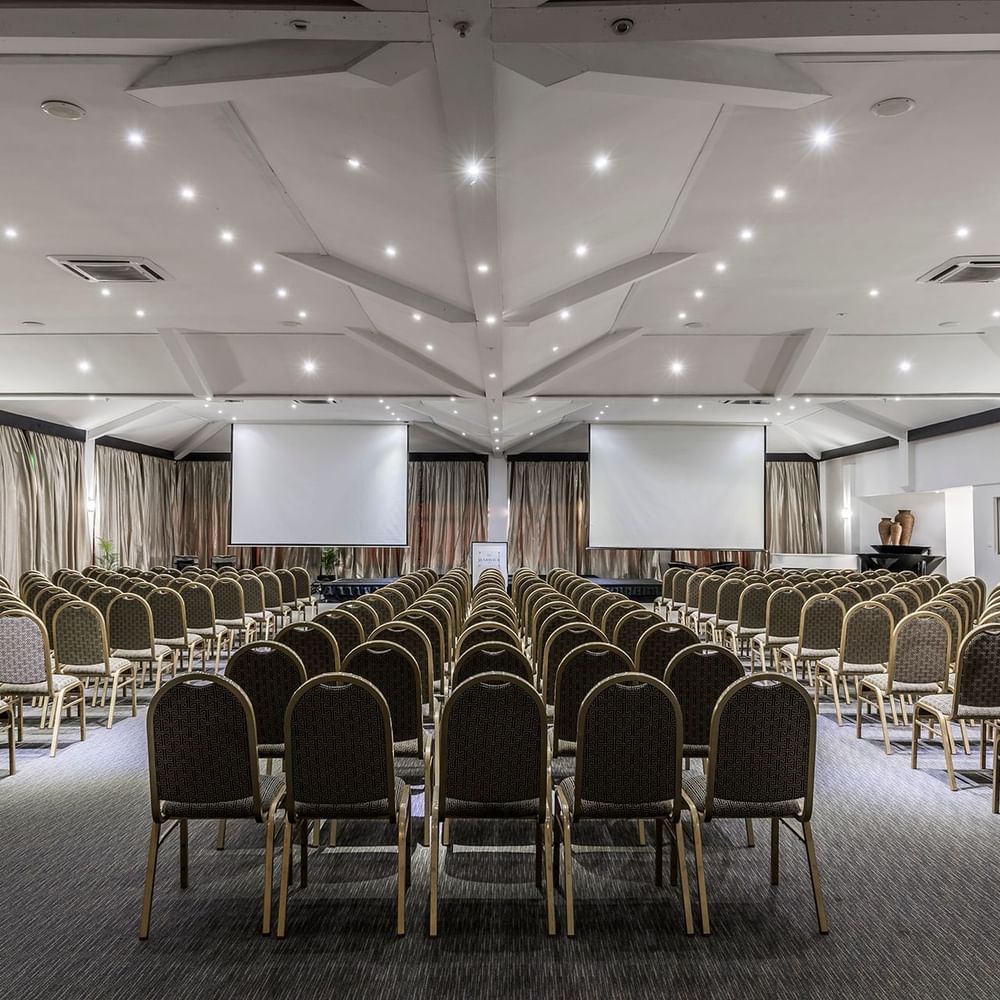Vusu Boardroom with rows of chairs by two large screens under a white vaulted ceiling at Warwick Fiji Resort and Spa