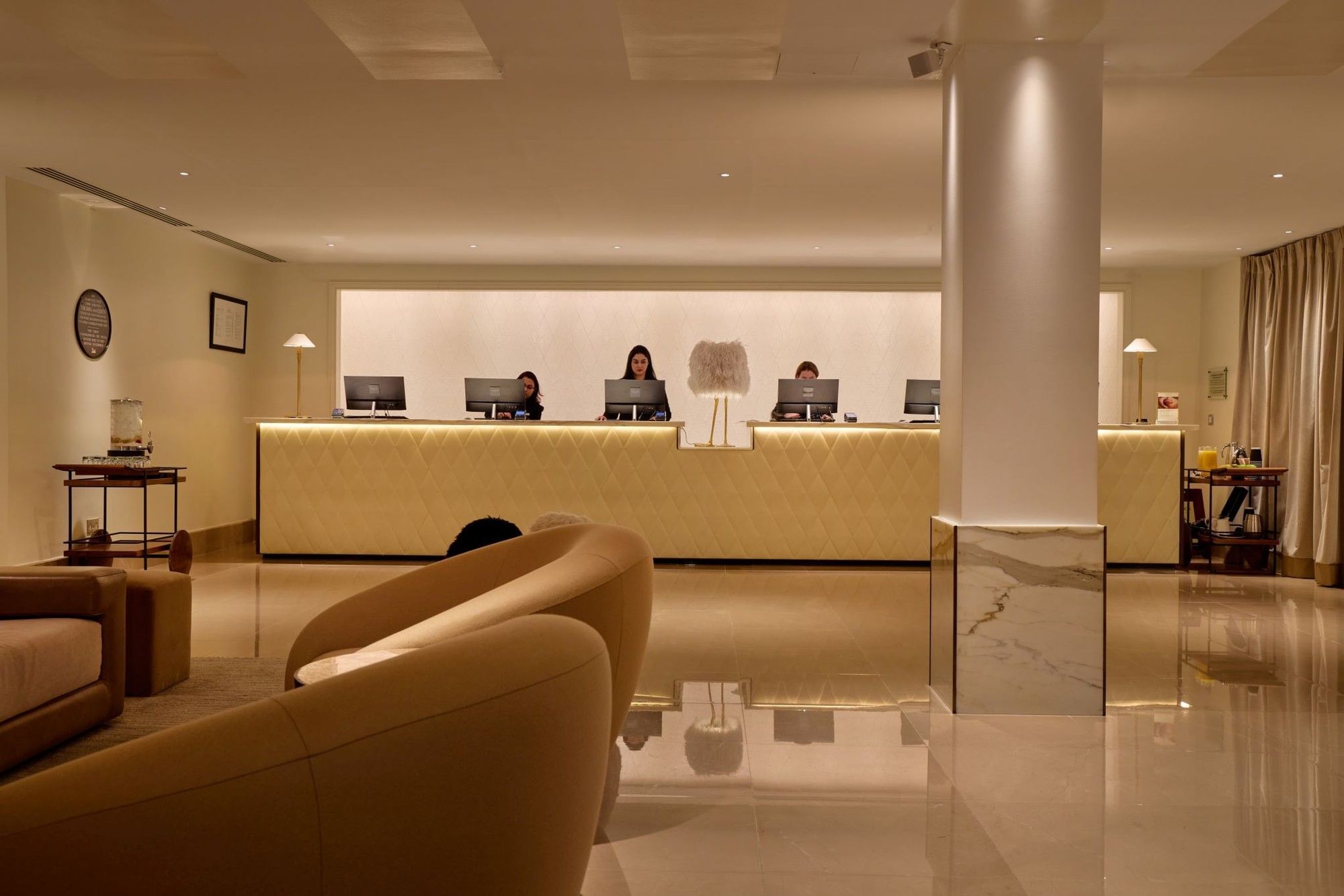 Elegant reception area with staff at counters and modern furnishings at The May Fair Hotel London.
