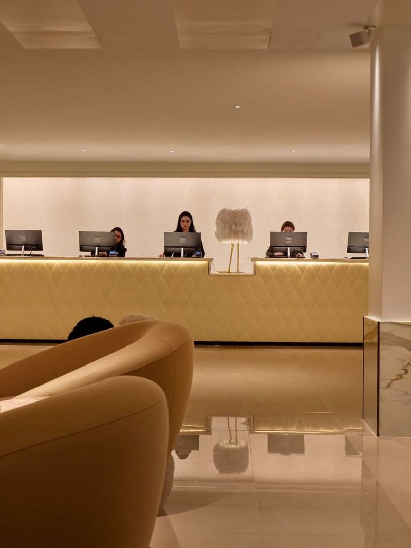 Elegant reception area with staff at counters and modern furnishings at The May Fair Hotel London.