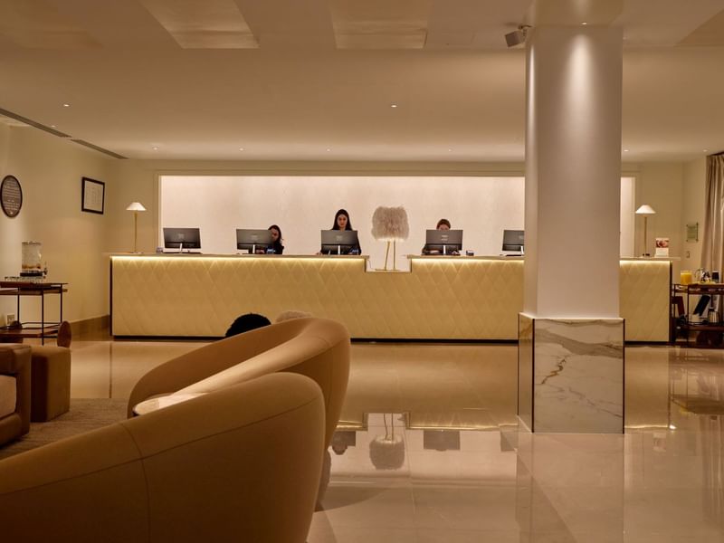 Elegant reception area with staff at counters and modern furnishings at The May Fair Hotel London.