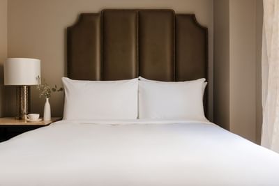Nightstand with a cup of coffee beside the cozy bed with cushioned headboard in Deluxe Queen Room at Hotel Bijou