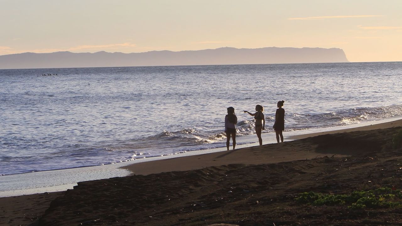 Three people by the ocean at sunset