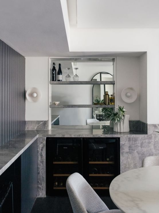 Elysium Suite at Elysium Manly featuring wine bottles on shelves by a dark panel wall, surrounding a marble table