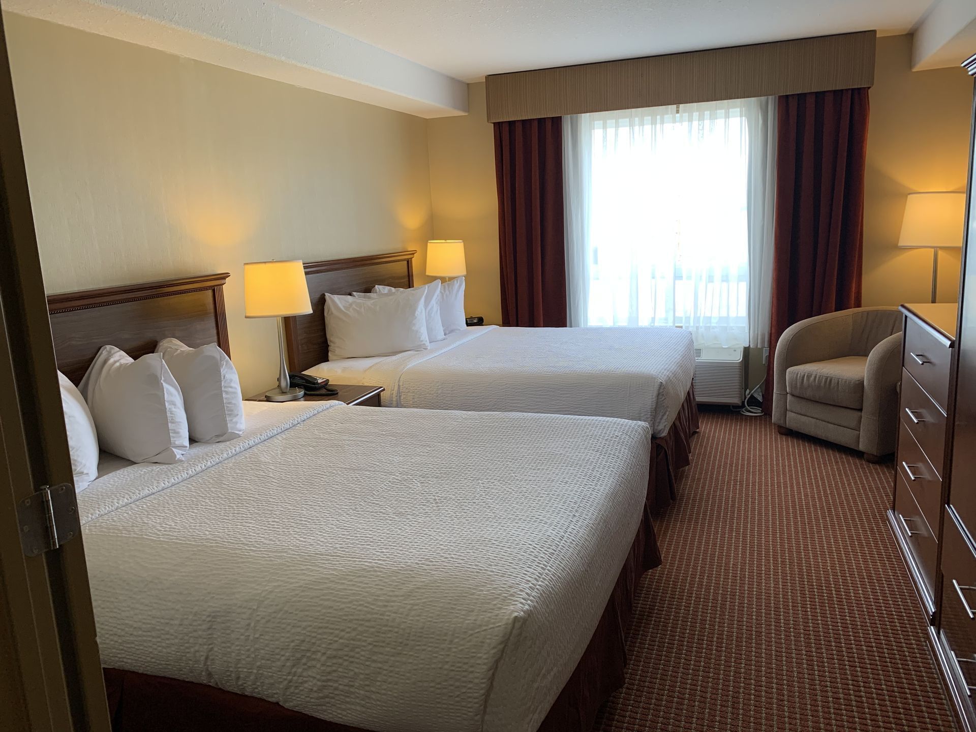 Lounger & nightstands by beds in Extended Stay Suite - 2 Queens at Merit Hotel & Suites
