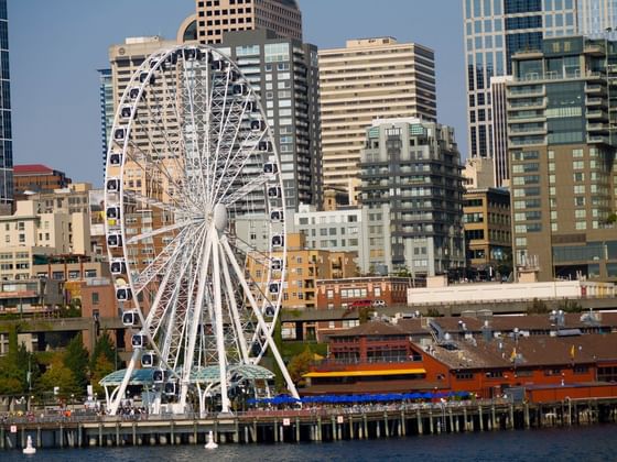 Large white Ferris wheel on a pier by the waterfront under a city skyline, near Paramount Hotel Seattle