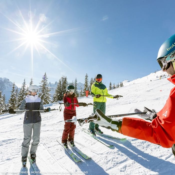 Quattro sciatori con attrezzatura completa, uno assistito da un istruttore, su una pista da sci innevata.
