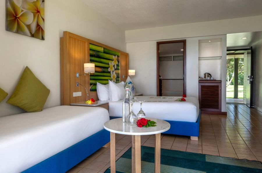 Water bottle on a table by a blue bed base under a tropical bamboo mural in Garden View Room at The Naviti Resort - Fiji