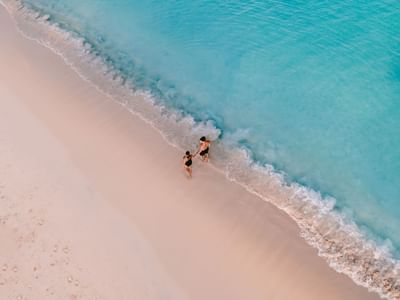 Aerial view of a couple holding hands in shallow turquoise waters near Amsterdam Manor Beach Resort