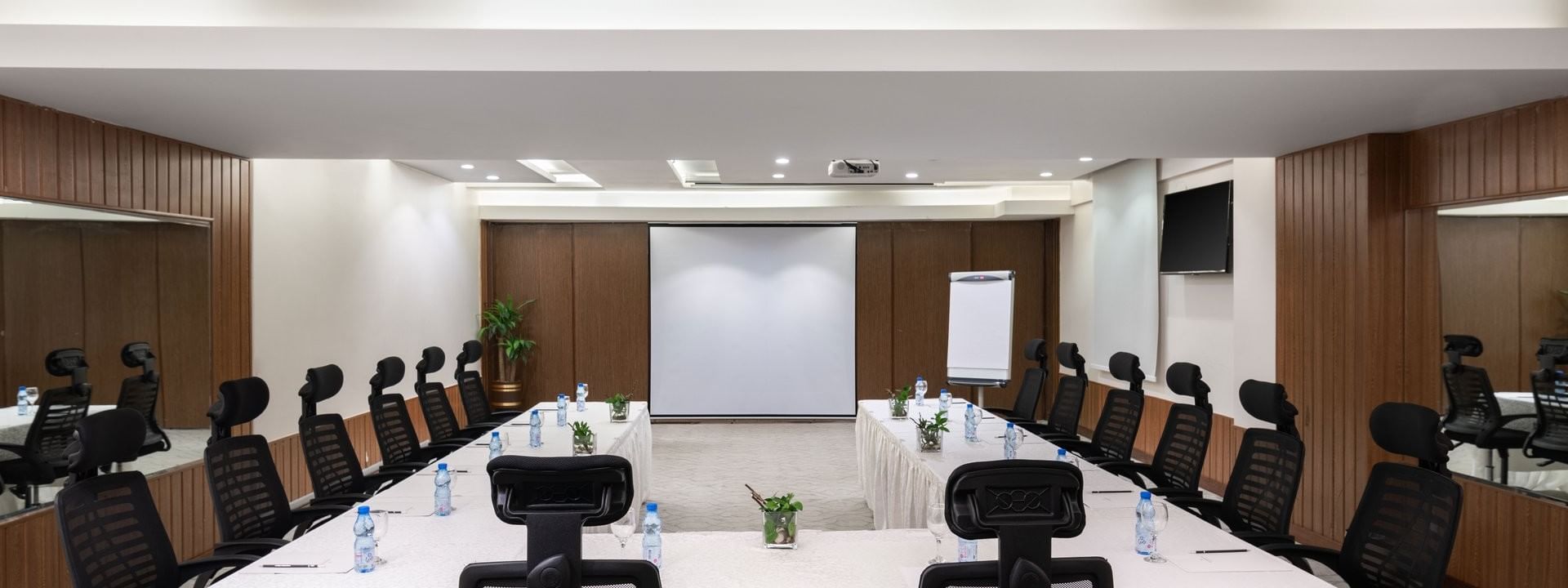 U-shaped table with black mesh chairs facing the projector screen in Meeting Room A at Warwick Hotel Jeddah
