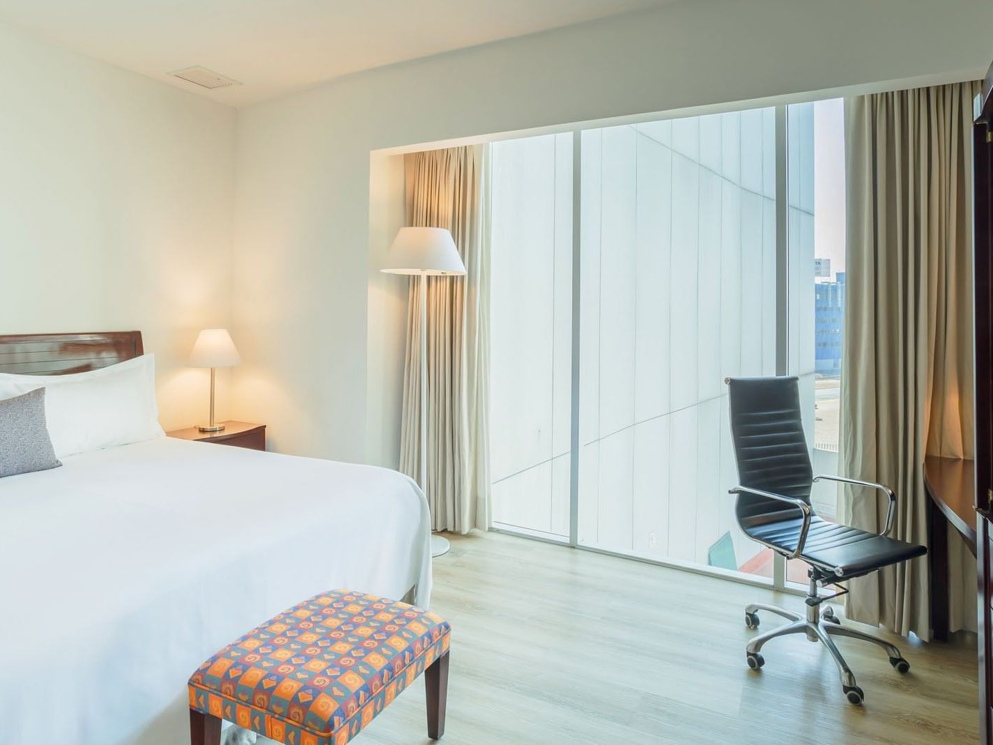King Junior Suite featuring a comfortable bed, a stylish bench, and floor-to-ceiling views at Camino Real Pachuca