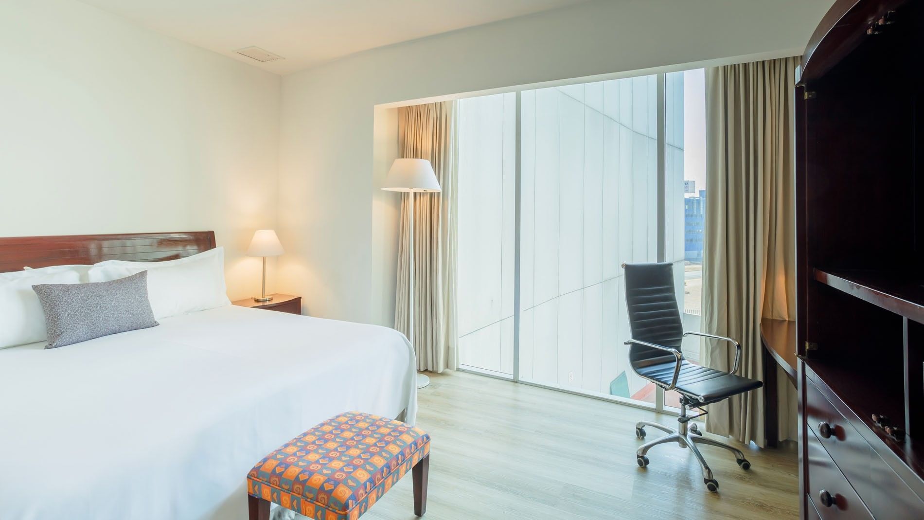 King Junior Suite featuring a comfortable bed, a stylish bench, and floor-to-ceiling views at Camino Real Pachuca
