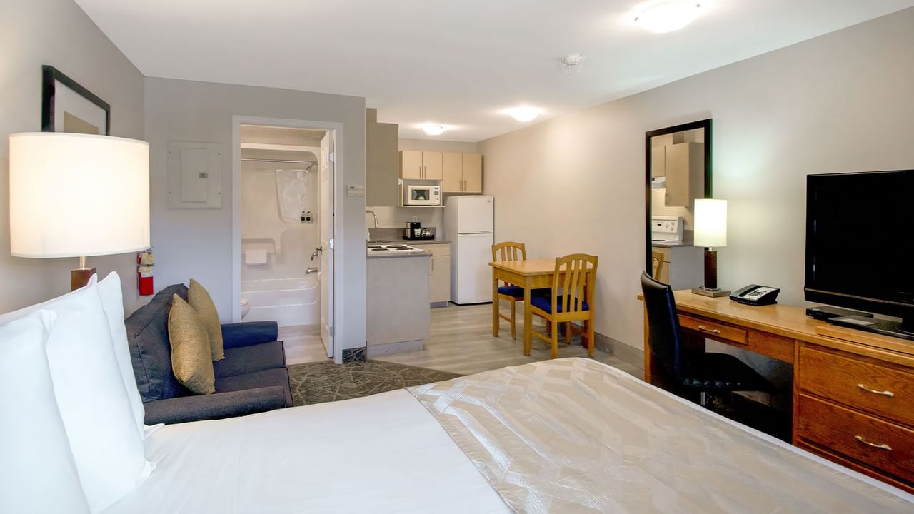 Hotel room with queen bed, sofa, TV, kitchen and bathroom.