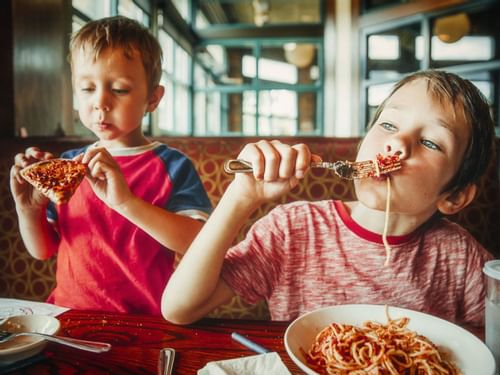 Two children eating spaghetti and pizza at The Reef Coco Beach