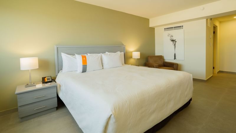 Comfortable bed with a side table and couch beneath stylish wall art in the King Executive Suite at Real Inn Mexicali