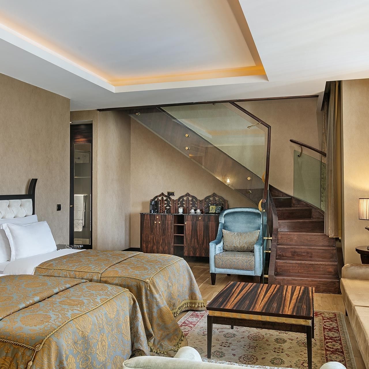 Гранд двухуровневый люкс в отеле Titanic Mardan Palace с двумя кроватями, диваном, стульями и стеклянной лестницей на верхний этаж