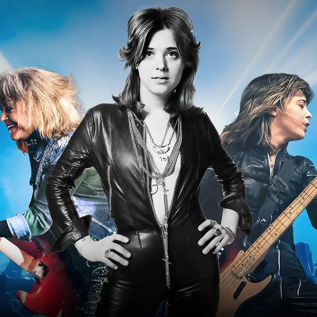 Suzi Quatro rocking out on stage with her bass guitar, surrounded by vibrant stage lighting