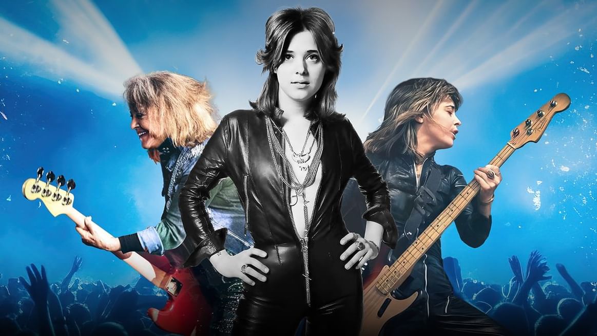 Suzi Quatro rocking out on stage with her bass guitar, surrounded by vibrant stage lighting