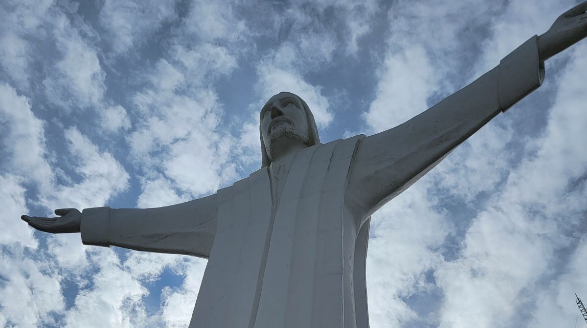 Colossal white statue of Christ with open arms near Camino Real Pedregal Mexico, set against a cloudy blue sky