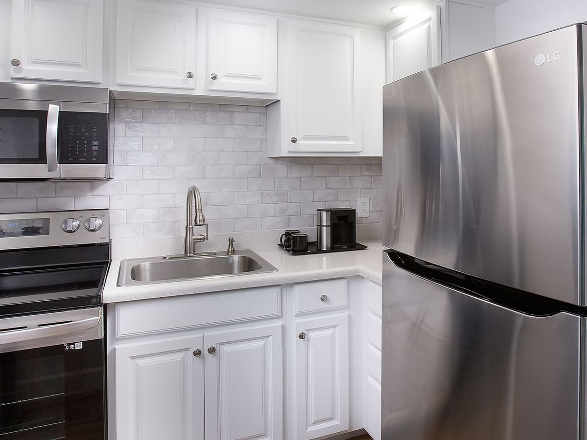 White kitchen with stainless steel appliances, sink, cabinets, and tiled backsplash.