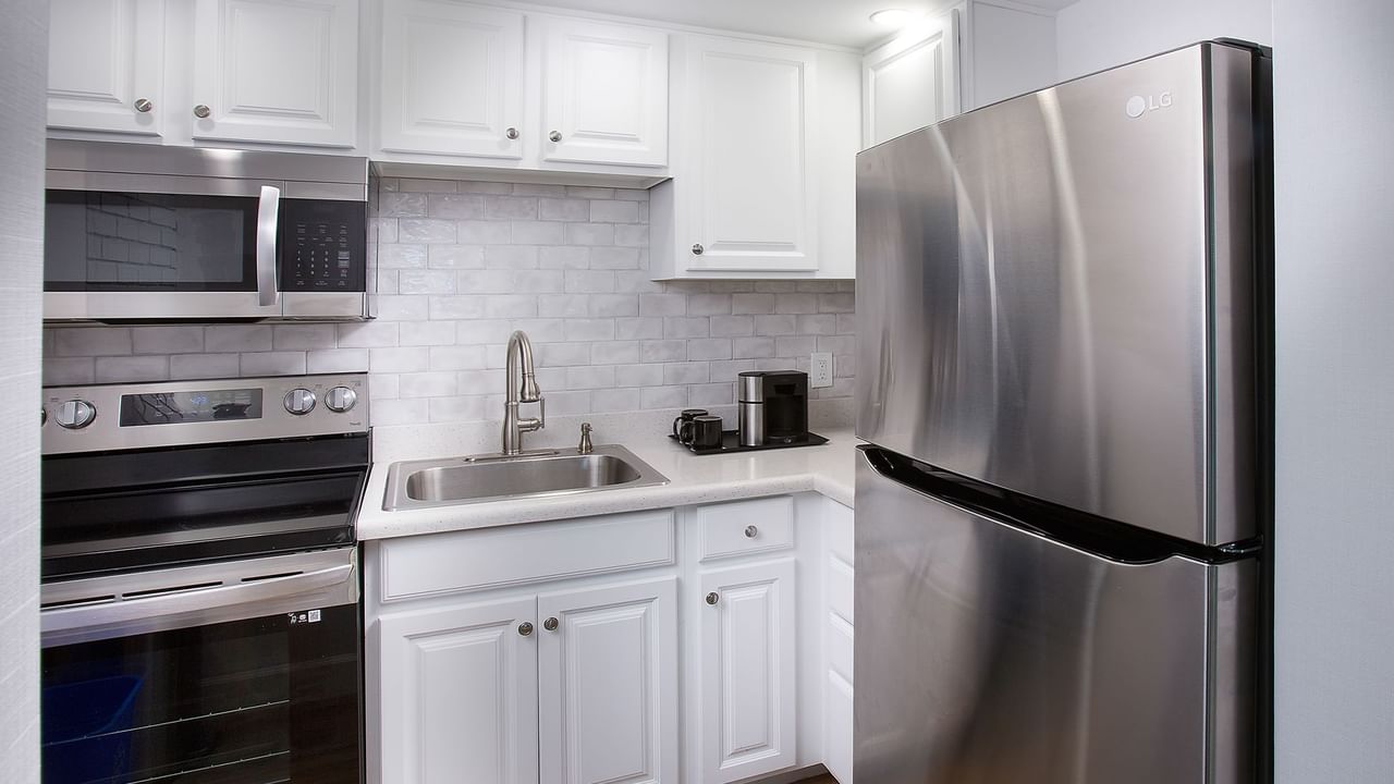 White kitchen with stainless steel appliances, sink, cabinets, and tiled backsplash.
