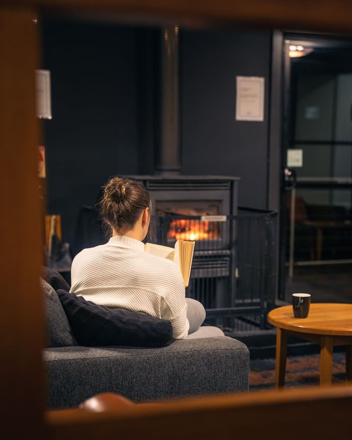 Lady reading a book by the fireplace at Cradle Mountain Hotel