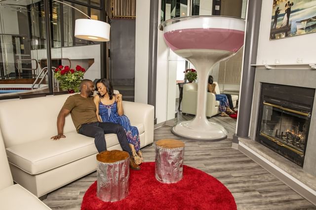 {Couple in a cozy lounge features a plush white sofa, stylish decor, and a warm fireplace at Cove Pocono Resorts}