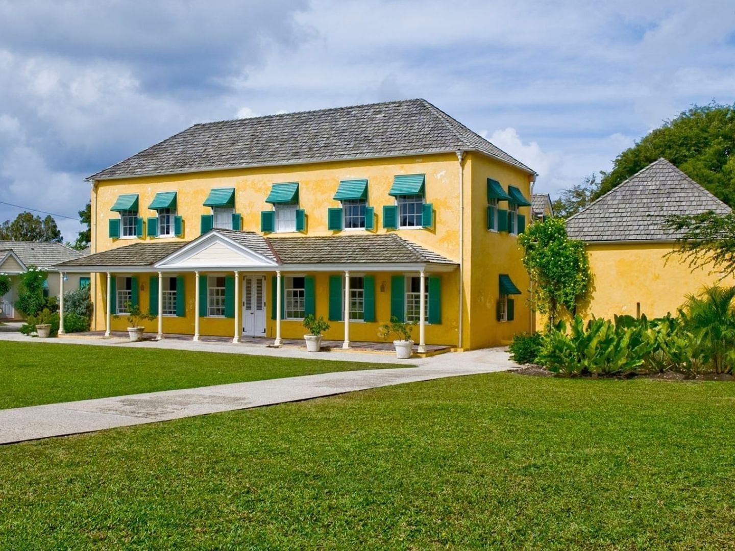 Yellow Savannah Beach Hotel with green shutters and gray roof surrounded by lush greenery and lawn.