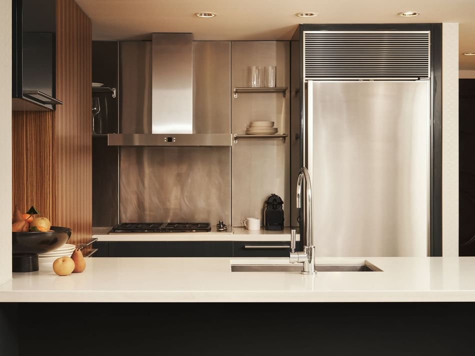 Modern kitchen with stainless steel appliances, white countertop, sink with faucet, and fruit bowl on the left.