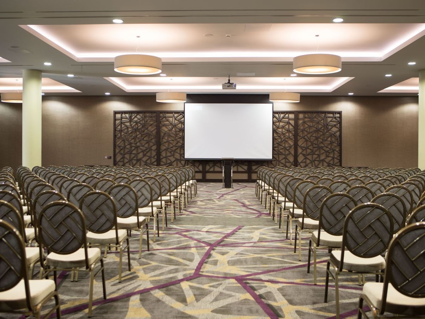 Rows of chairs facing a large projection screen, illuminated by stylish ceiling lights at the Heston Hyde Hotel