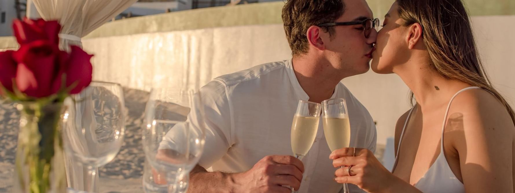 A romantic couple shares a kiss and champagne toast at an outdoor table near the Marquis Los Cabos Resort