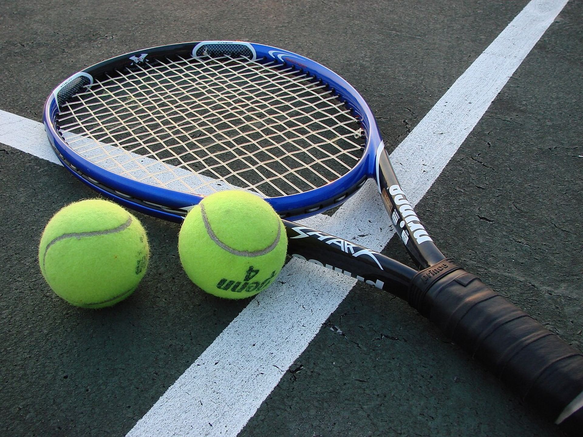 Blue tennis racket resting on a court next to two bright green tennis balls at Windsong Resort On The Reef