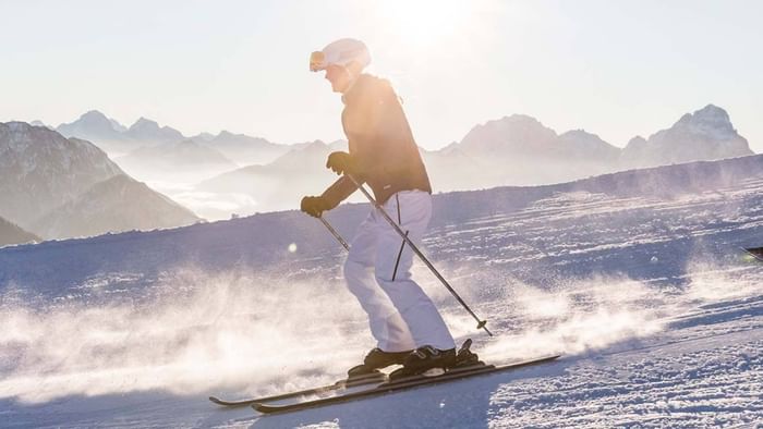 Skifahrer in weißer Hose und schwarzer Jacke auf Skiern in den Alpen mit Nebel und Sonnenlicht.
