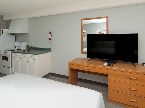 Guest room with white bedding, kitchenette, flat-screen TV, and wooden dresser.