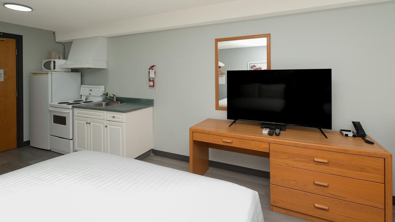 Guest room with white bedding, kitchenette, flat-screen TV, and wooden dresser.