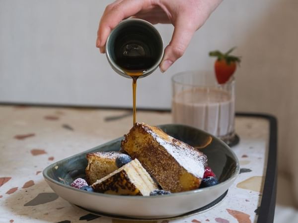 Pouring syrup onto French toast with berries on a plate at Almanac Palais Vienna