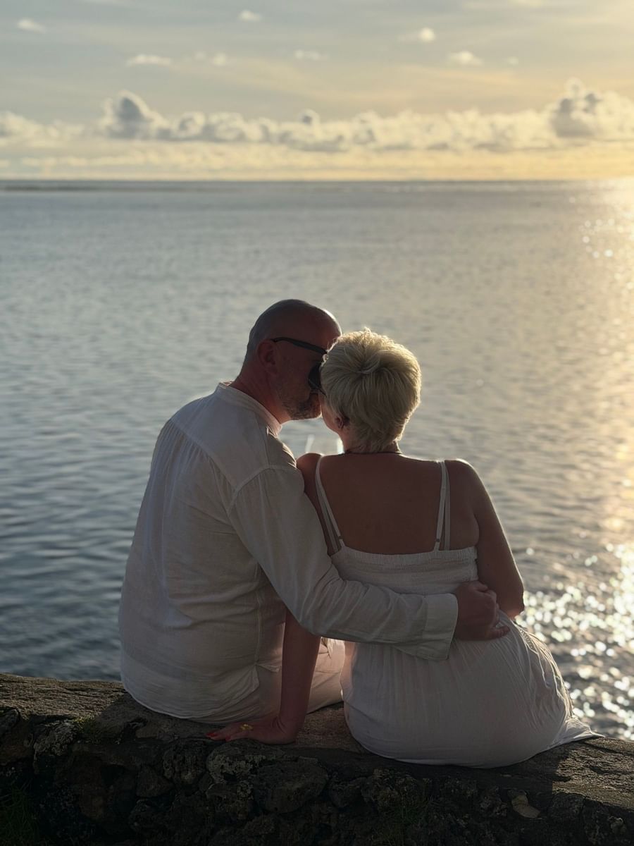 Couple in white clothing sitting together on the edge of a rock overlooking the ocean.