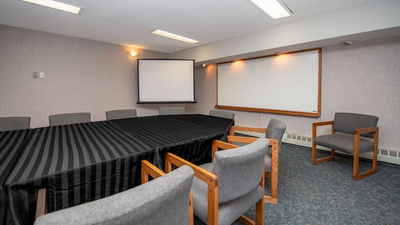 Meeting room with a long table, chairs, projector screen, and whiteboard on the wall.