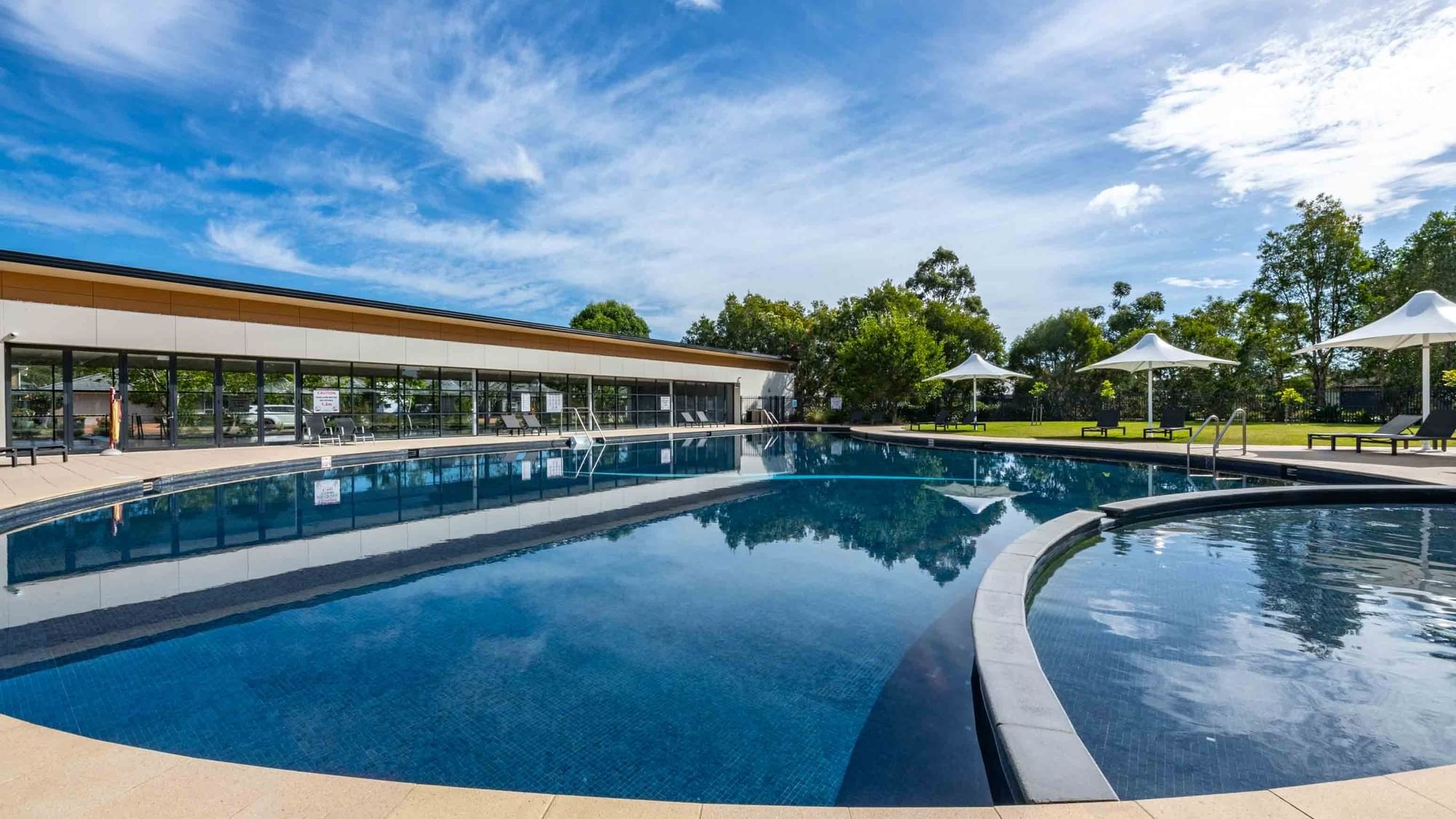 Outdoor pool with sun loungers and white parasols at Mercure Kooindah Waters