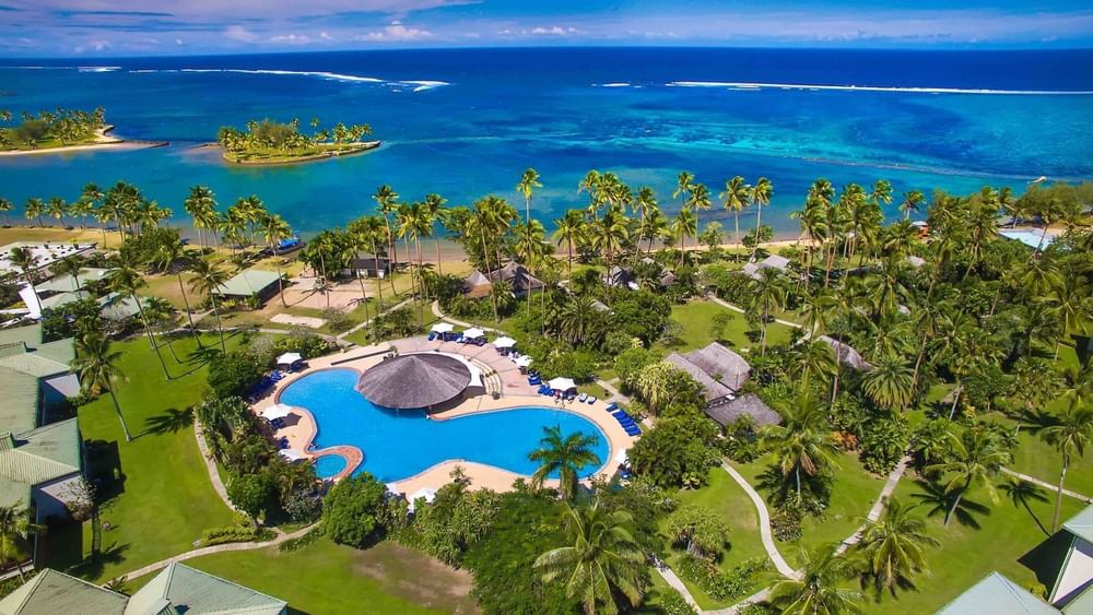 View of The Naviti Resort with blue pool by a thatched hut surrounding a lush garden at Warwick Fiji Resort and Spa