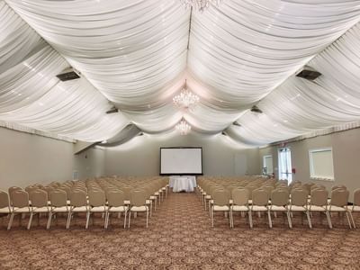 Theater-style set up with rows of chairs facing a large screen, and elegant drapes in a ballroom at Lake Natoma Inn