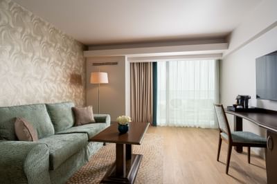 Room featuring a green sofa, wooden table, modern lamp, and a desk area with a TV at Ana Hotels Europa Eforie Nord