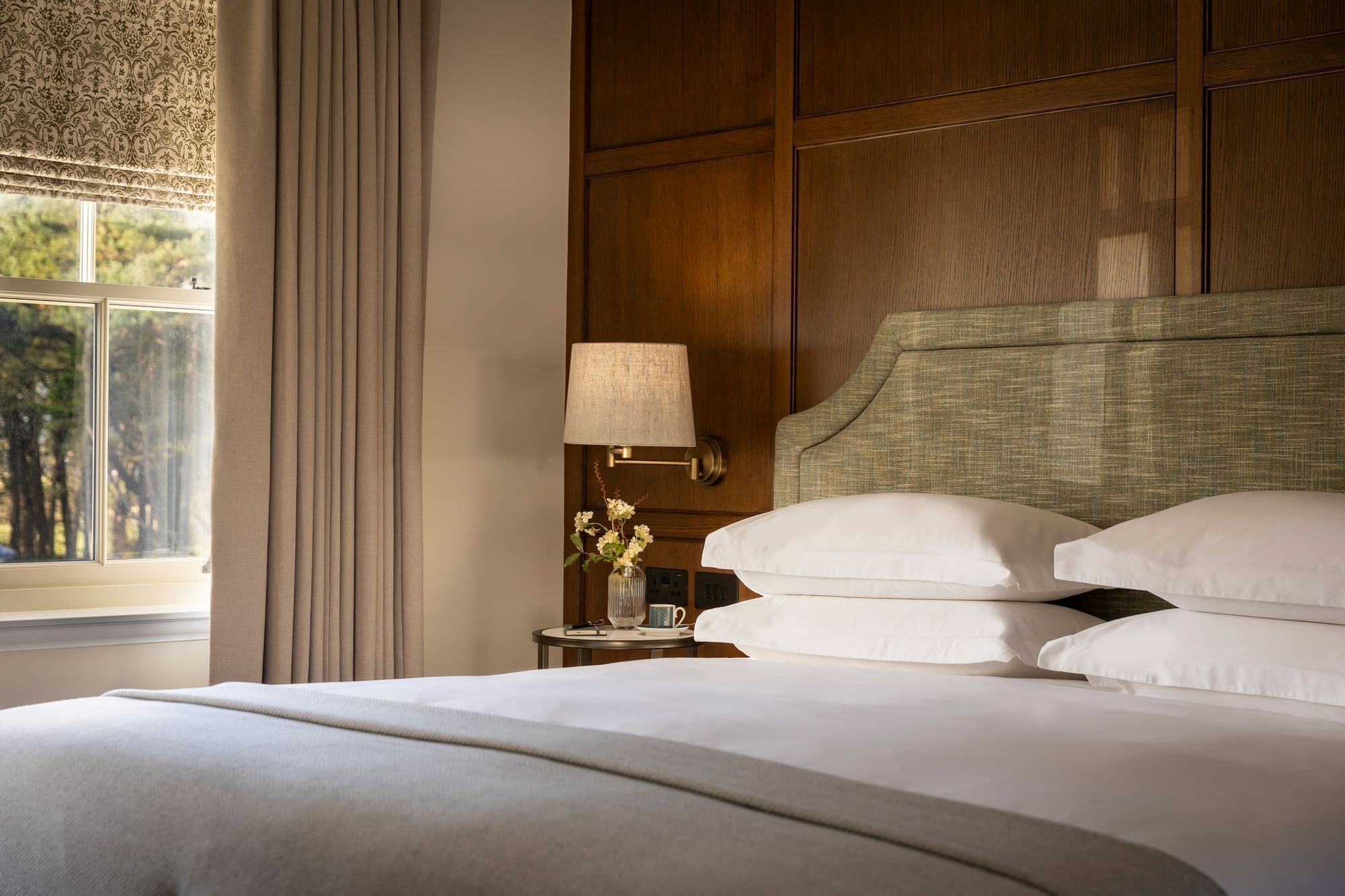 A luxury guest bedroom at Dunluce Lodge with a cozy green-tufted headboard, crisp white bedding, and light from a window