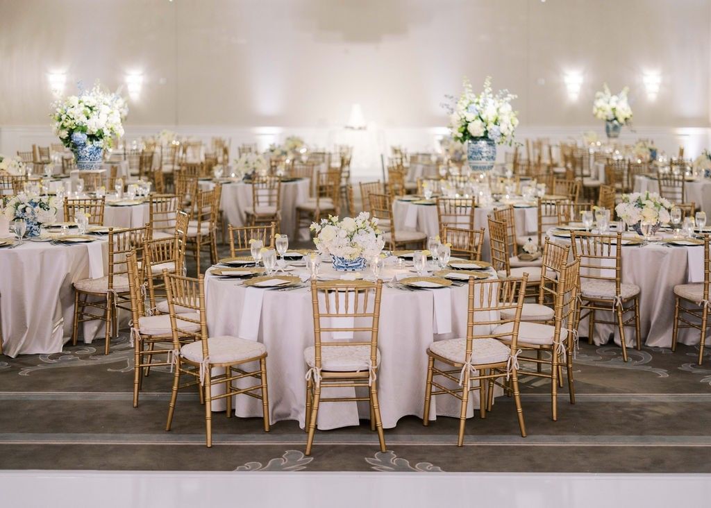 Gold chairs by round tables under floral centerpieces in a bright ballroom at Warwick Melrose Dallas