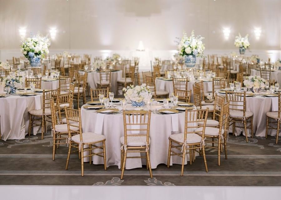 Gold chairs by round tables under floral centerpieces in a bright ballroom at Warwick Melrose Dallas