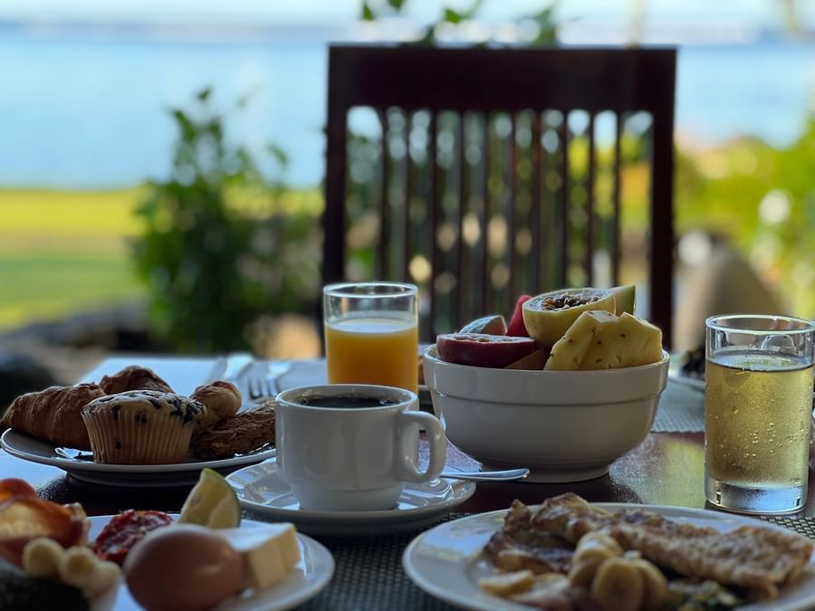 Plates of breakfast foods, fruit bowl, and drinks on table at Warwick Fiji Resort and Spa.