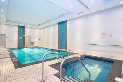 Indoor pool with adjacent hot tub, metal handrails and tiled floor at Winnipeg Hotels near airport